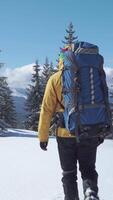 Backpacker hiking in snowy mountains, A traveler with a large backpack hikes through a snowy forest with mountain views. Vertical footage video