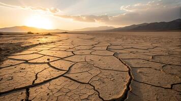 The sun is setting over a dry desert with cracked ground photo