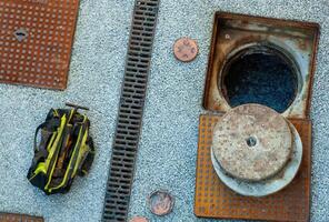 Plumber bag and open manhole on concrete floor with drainage grid photo