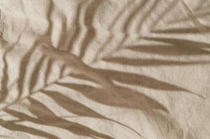 Tropical palm tree leaves shadow on sand color linen background. Minimal summer concept. An original backdrop image with a play of light and shadow. Creative copy space. Summer aesthetic. Flat lay. photo