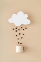 Creative layout made of cloud shape paper card note, coffee beans rain and coffee cup on beige background. Minimal concept. Trendy weather idea. Coffee aesthetic. Flat lay style. Top view banner. photo