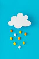 Creative composition made of cloud shape paper card note and colorful Easter eggs rain on blue background. Minimal Easter concept. Festive holiday layout. Easter aesthetic. Flat lay style. Top view. photo