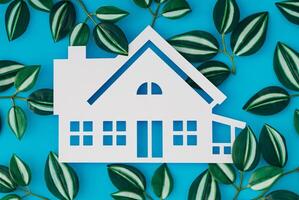 House shaped white paper cutout and colorful leaves on light blue background. Minimal concept. Flat lay style. Top view banner. photo