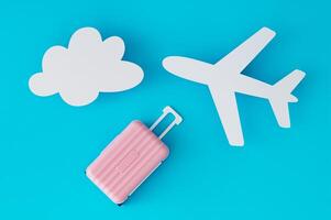 Travel concept with pink suitcase, cloud and plane paper cards on light blue background. Trendy vacation idea. Unique holiday flat lay. Creative copy space. Top view banner. photo