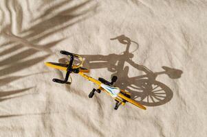 Summer day scene with yellow bicycle on sand color linen background. An original background image with a play of light and shadow. Minimal bicycling concept. Creative sport bike composition. Flat lay. photo