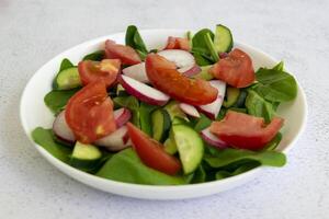 Raw fresh green healthy organic salad of spinach, cucumber, tomato and radish in white bowl on table top view on grey background. photo