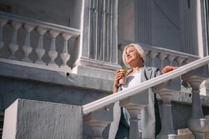 A woman is standing on a white staircase with a cup in her hand. She is smiling and looking up at the sky. photo