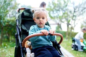 Little girl sits in the garden in a stroller, holding the handle photo