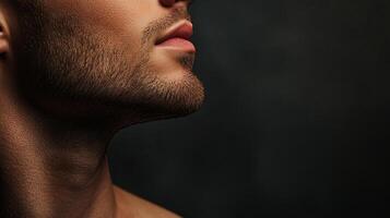 Close-up of a man's profile showcasing his jawline, beard, and lips, set against a dark background. The lighting highlights facial details. photo