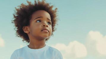 A young child with afro hair gazes up at the sky, lost in thought. The picture portrays innocence and the wonder of youth. photo