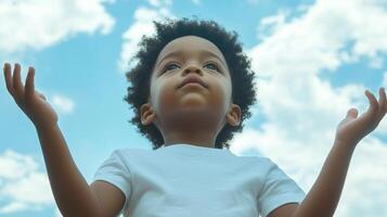 A young child with curly hair looks upwards toward a blue sky dotted with fluffy clouds, arms raised in a gesture of wonder or hope. photo