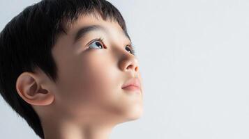 Young boy looking upwards with a hopeful expression against a plain background, capturing innocence and a sense of aspiration. photo