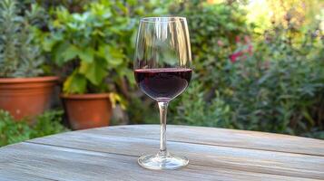 A glass of red liquid on a wooden table, surrounded by lush greenery, bathed in soft sunlight, creating a serene, natural setting. photo