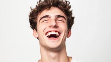 A young man with curly hair, eyes closed, and laughing heartily, showcasing genuine happiness and joy in a bright, clean studio setting. photo
