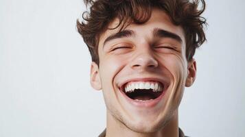A young man with curly brown hair is bursting with joy, eyes closed, and a wide, radiant smile against a neutral backdrop of white. photo