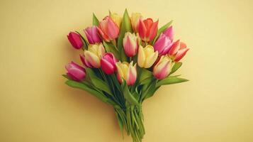 A vibrant bouquet of tulips bursts with color, showcasing shades of pink, yellow, and red against a soft, yellow background. photo