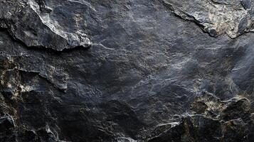 Detailed view of a dark, textured rock face. The rough surface highlights the natural patterns and age of the stone formation. photo