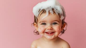 A happy baby with shampoo suds on her head smiles brightly against a solid pink background, showcasing innocence and joyful cleanliness. photo