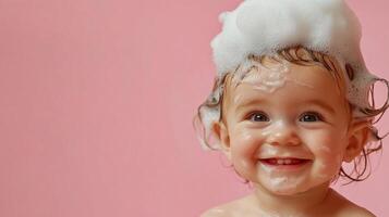 A happy baby is covered in bubbles while having a bath. The little toddler is smiling and enjoying bath time on pink background. photo