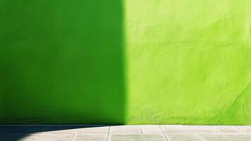 A vibrant green painted wall is partially shadowed, creating a strong contrast and dynamic visual effect on concrete tiles. photo