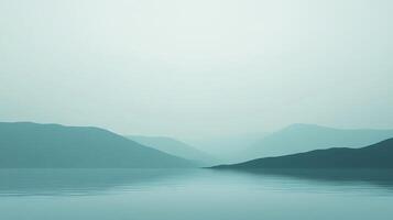 A tranquil view of a mist-covered landscape, showcasing soft hills reflected in a serene body of water, creating a beautifully peaceful atmosphere. photo
