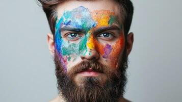 A man with a full beard and colorful paint on his face gazes directly at the camera, creating a striking and artistic portrait. photo