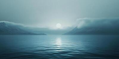 Mist drifts over the blue water, obscuring mountain peaks as the sun reflects on the serene ocean's surface in the distance. photo