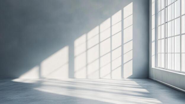 Sunlight streams through a large window, casting a geometric pattern on the gray walls and floor of an empty room, creating a peaceful ambiance. photo