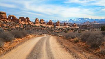 Scenic desert landscape with a dirt road winding through red rock formations against a backdrop of distant snow-capped mountains. photo