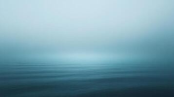 A serene expanse of water meets a hazy sky, where the horizon blends seamlessly into a gradient of blue, evoking calmness and vastness. photo