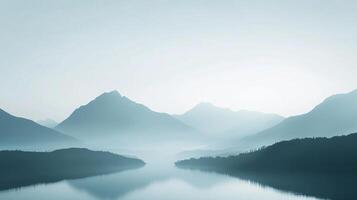 Serene mountain range reflected in calm waters, shrouded in a delicate, atmospheric mist creating a peaceful, dreamlike landscape. photo