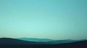 Silhouette of rolling hills under an expansive teal sky. A gradient of color creates a serene and peaceful atmosphere. Nature's beauty is displayed. photo