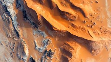 Aerial view of stunning desert sand dunes with warm, orange hues and textured patterns, contrasted by rocky terrain, creating dynamic scenery. photo