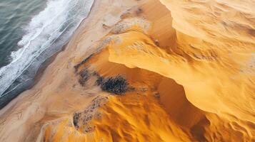 Aerial view of towering sand dunes meeting the ocean, creating a stunning contrast of arid desert and crashing waves. photo