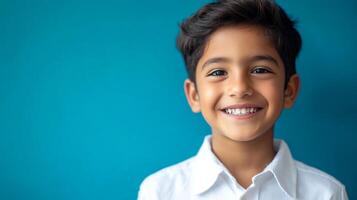 Smiling young boy with a bright, happy expression against a solid blue background, wearing a white collared shirt. Joyful and positive vibes. photo