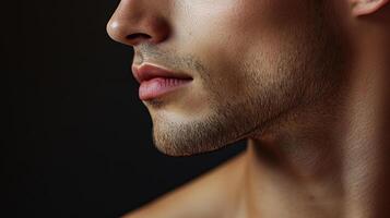 Close-up profile of a man's face against a black background. Focus is on his lips, beard, and jawline, highlighting grooming and skincare. photo