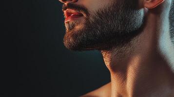 Close-up profile of a person's face highlighting their well-groomed beard and neck against a dark backdrop showcasing light contrast. photo