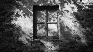 Window on stone wall with leaf shadows, black and white. Stark contrast highlights textures and creates a sense of rustic tranquility. photo