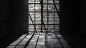 Sunlight streams through a barred window, casting stark shadows across the textured brick wall and tiled floor in an otherwise dark space. photo