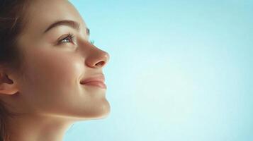 Serene portrait of a woman with a gentle smile, gazing upwards against a light blue backdrop, embodying peace and hopeful anticipation. photo