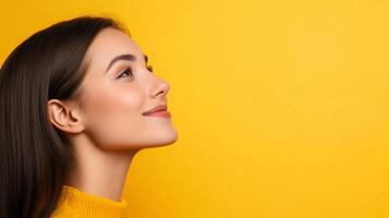 Young woman looking upwards against a bright yellow background. She is smiling and seems hopeful, suggesting optimism and positive thinking. photo