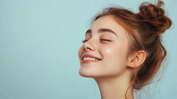 Smiling young woman with closed eyes, freckles, and a messy bun, basking in the sun with a serene facial expression, against a soft blue background. photo