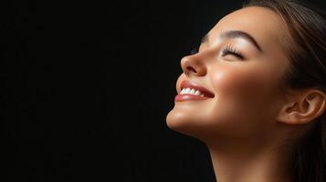 Radiant beauty radiates from the face of a woman, her complexion glowing against the dark background, smile, and perfect skin. photo