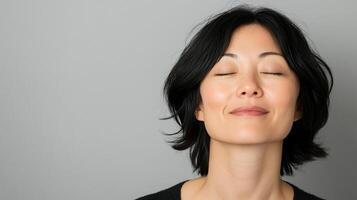 Serene woman with closed eyes and a gentle smile, radiating tranquility and inner peace against a neutral background. Feeling calm and centered. photo