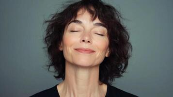 A woman with dark hair and eyes closed seems to be enjoying a moment of peace and serenity against a muted blue-grey background. photo
