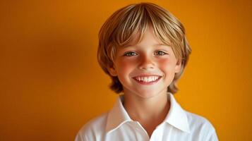 A joyful young boy with blond hair and a bright smile poses against a vibrant orange backdrop, radiating happiness and innocence. photo