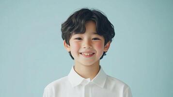 Portrait of smiling young boy with wavy dark hair wearing a white shirt against a simple light blue background for studio portraiture. photo