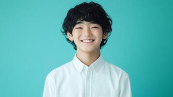 Happy young boy with dark curly hair and a white button-down shirt, smiling brightly against a vibrant aqua background. photo