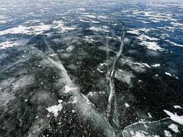 Frozen lake surface with cracks and scattered snow patterns displayed photo