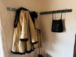 Traditional wool coats and embroidered bag hanging on rustic wooden rack indoors photo